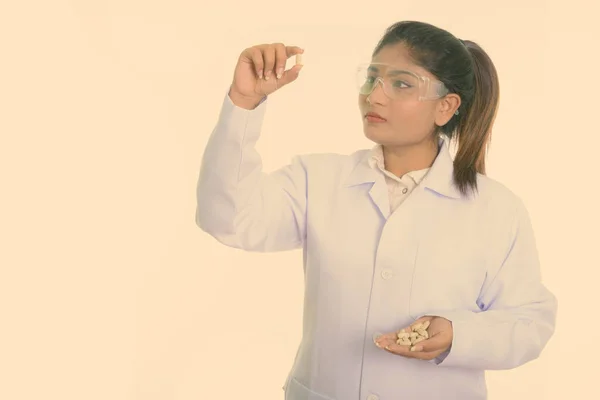 Estudio de inyección de grasa joven médico mujer persa mirando tabletas de vitaminas mientras usa gafas de protección aisladas contra el fondo blanco — Foto de Stock