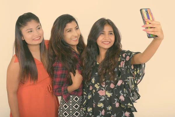 Tres felices jóvenes amigas persas sonriendo mientras toman una foto selfie con teléfono móvil togther sobre fondo blanco —  Fotos de Stock