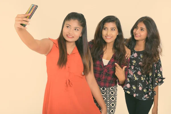 Captura de estudio de tres felices jóvenes amigas persas sonriendo mientras toman una foto selfie con teléfono móvil togther sobre fondo blanco —  Fotos de Stock