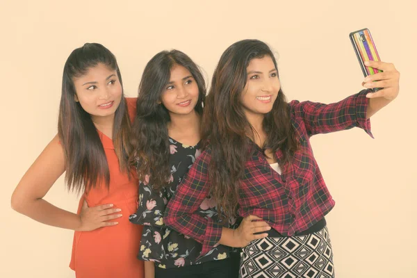 Estudio de tres felices jóvenes amigas persas sonriendo y posando mientras toman una foto selfie con teléfono móvil togther sobre fondo blanco —  Fotos de Stock