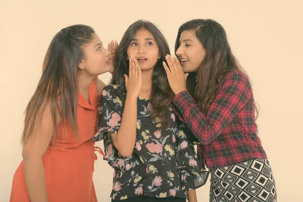 Studio shot of young Persian woman looking shocked with both friends whispering on each side