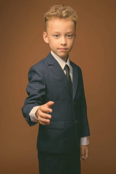 Młody chłopiec jako biznesmen na brązowym tle — Zdjęcie stockowe