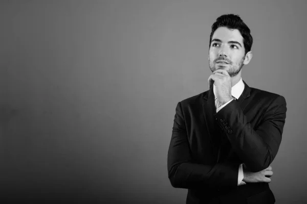 Ung stilig affärsman i kostym mot grå bakgrund — Stockfoto
