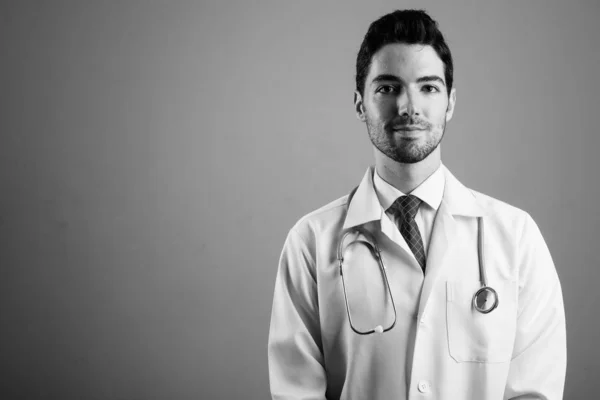 Portrét mladého pohledného muže lékaře na šedém pozadí — Stock fotografie