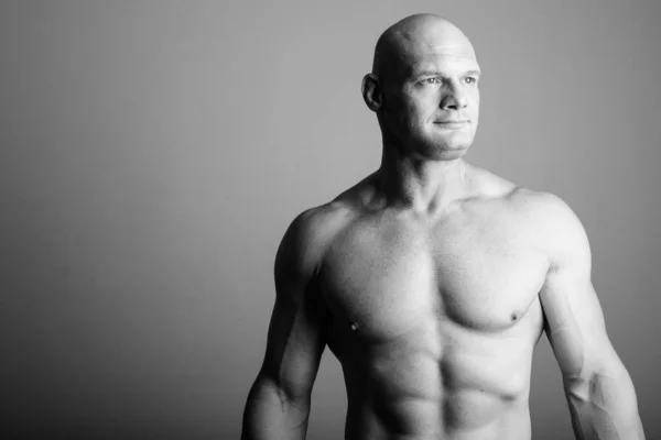 Plešatý svalnatý muž bez košile proti šedému pozadí — Stock fotografie