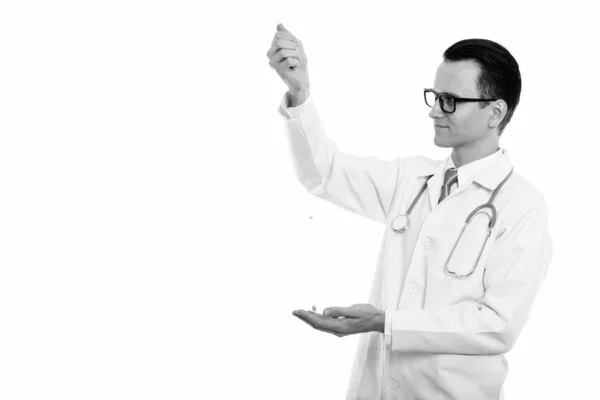 Studio shot of young handsome man doctor slipping vitamin tablets from hand — Stock Photo, Image