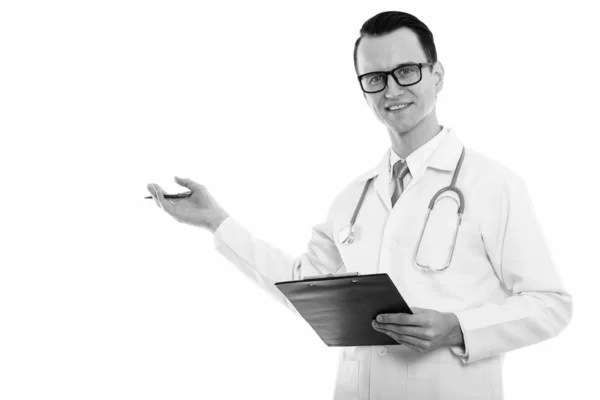 Студийный снимок молодого счастливого человека доктор улыбается, держа планшет и ручку, показывая что-то — стоковое фото