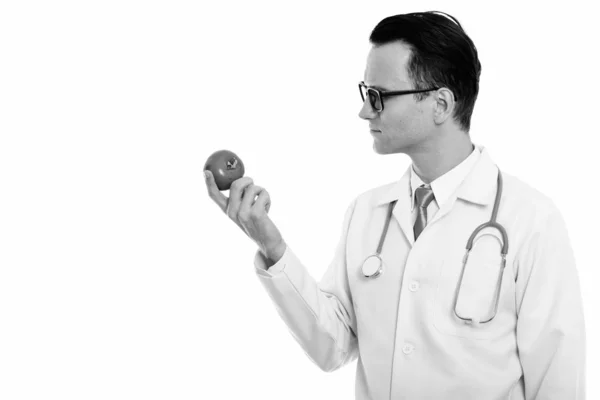 Profile view of young handsome man doctor holding red tomato — Stock Photo, Image