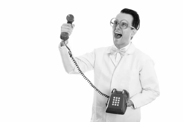 Studio shot of happy crazy man docteur souriant et pensant tout en donnant vieux téléphone — Photo