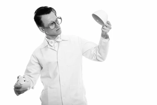 Studio shot de jeune homme fou médecin tenant tirelire et tasse de café vide à l'envers — Photo