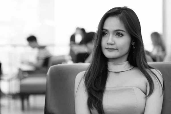 Zamyšlený mladý krásný asijské žena sedí uvnitř nákupního centra — Stock fotografie
