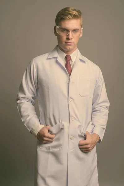 Νεαρός όμορφος άντρας γιατρός με ξανθά μαλλιά σε γκρι φόντο — Φωτογραφία Αρχείου