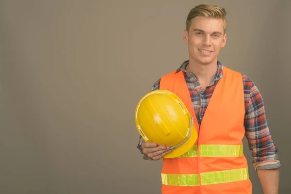 Joven hombre guapo trabajador de la construcción con el pelo rubio sobre fondo gris — Foto de Stock