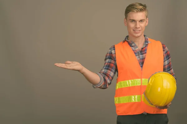 Jovem homem bonito trabalhador da construção com cabelo loiro contra fundo cinza — Fotografia de Stock