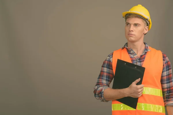 Joven hombre guapo trabajador de la construcción contra el fondo gris —  Fotos de Stock