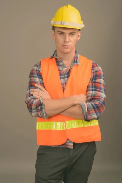 Genç yakışıklı adam inşaat işçisi gri bir arka plana dayanır — Stok fotoğraf