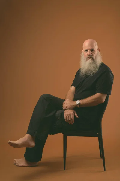 Зрелый лысый мужчина с длинной бородой сидит на стуле в черно-белом — стоковое фото