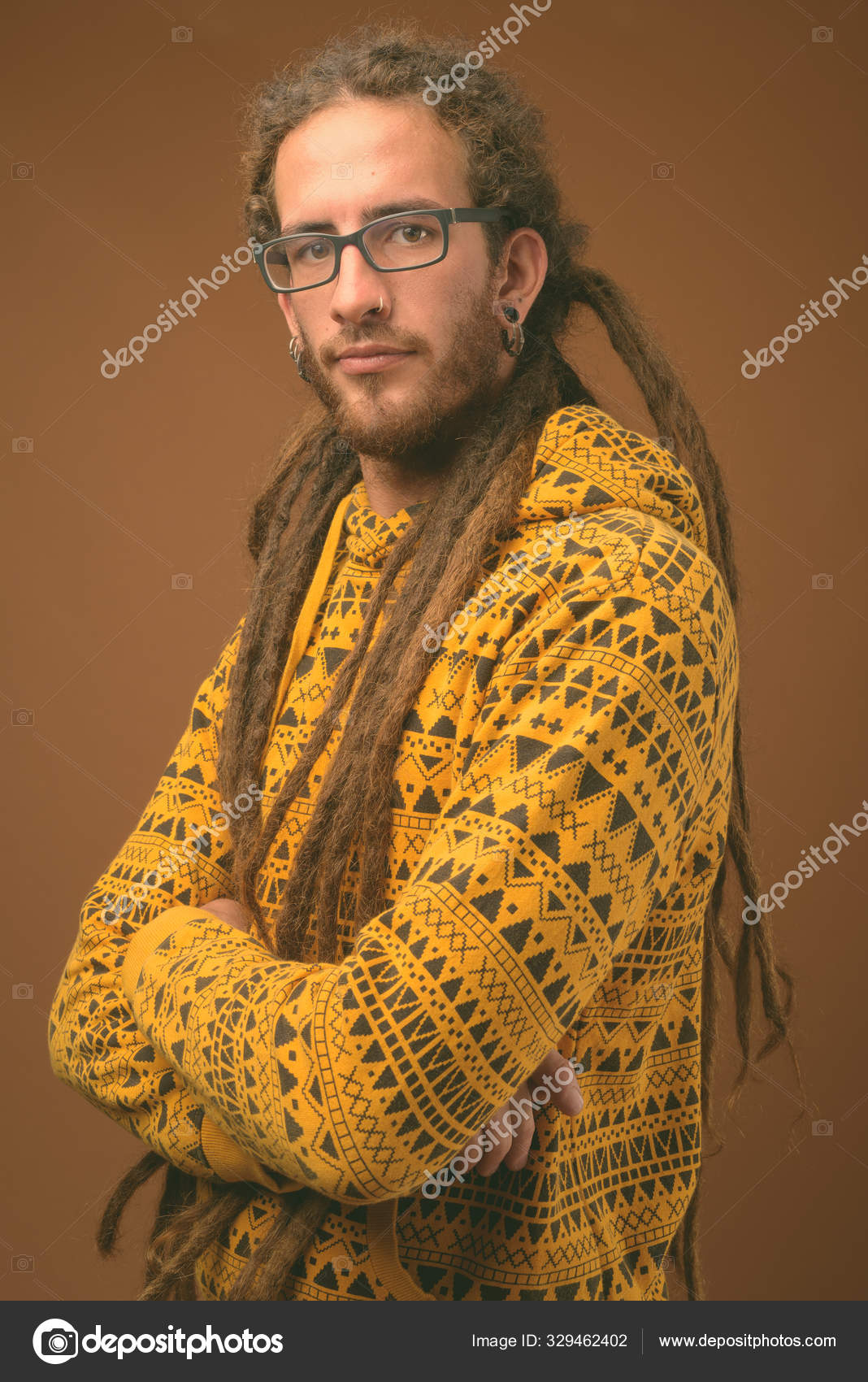 Young handsome Hispanic man with dreadlocks against brown background