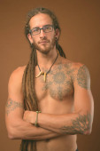 junger hübscher hispanischer Mann mit Dreadlocks ohne Hemd vor braunem Hintergrund