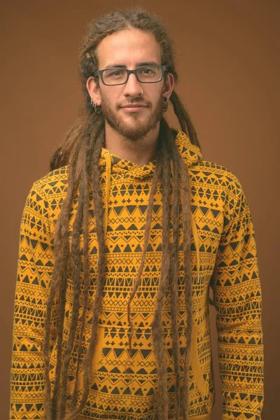 Homem hispânico bonito jovem com dreadlocks contra fundo marrom — Fotografia de Stock