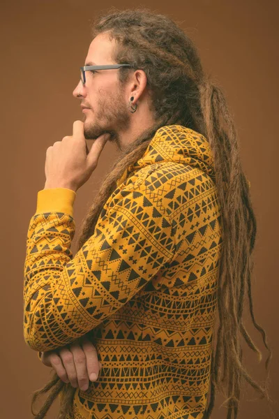 Joven hombre hispano guapo con rastas sobre fondo marrón — Foto de Stock