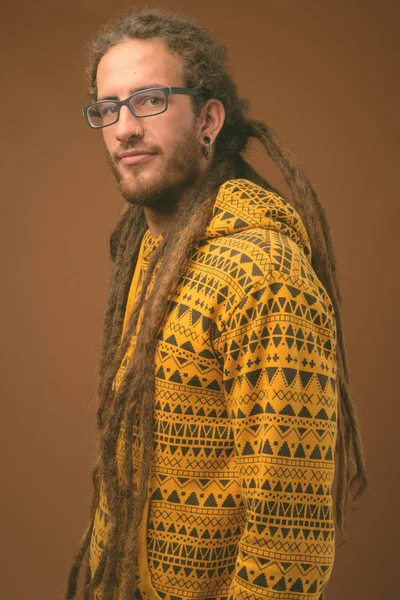 Joven hombre hispano guapo con rastas sobre fondo marrón — Foto de Stock