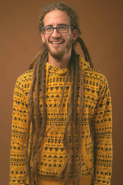 Homem hispânico bonito jovem com dreadlocks contra fundo marrom — Fotografia de Stock