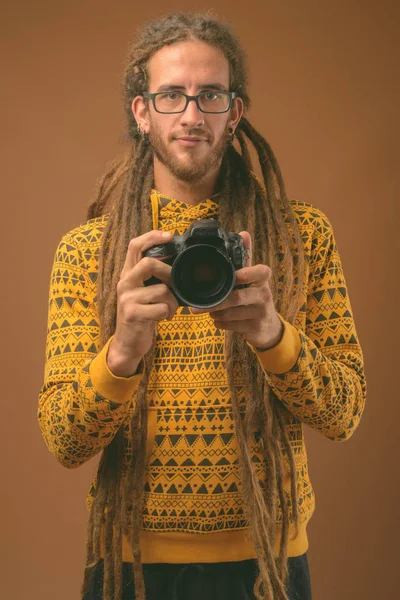 Joven hombre hispano guapo con rastas sobre fondo marrón — Foto de Stock