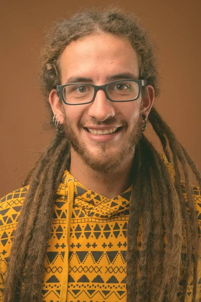 Joven hombre hispano guapo con rastas sobre fondo marrón — Foto de Stock