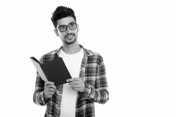 Studio shot di giovane uomo persiano che indossa occhiali da vista e tenendo libro mentre pensa — Foto Stock