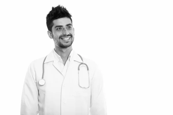 Studio shot of young happy Persian man doctor souriant et réfléchissant tout en levant les yeux — Photo