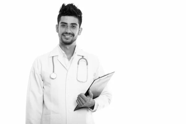 Studio shot of young happy Persian man doctor smiling while holding clipboard — Stock Photo, Image