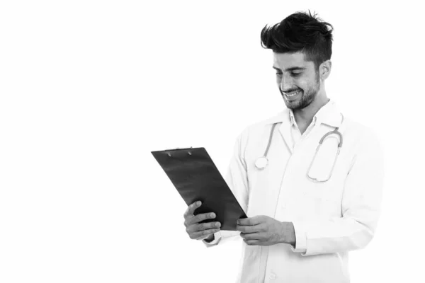 Studio shot of young happy Persian man doctor smiling while looking at clipboard — Stock Photo, Image