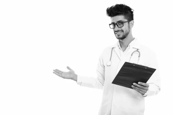 Joven hombre persa feliz médico sonriendo mientras sostiene el portapapeles y mostrando algo —  Fotos de Stock