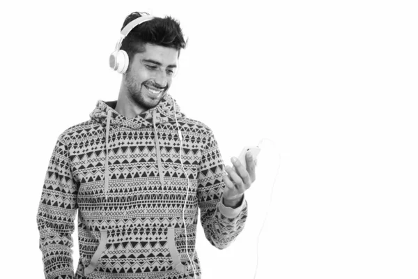 Estúdio tiro de jovem feliz persa homem sorrindo e ouvir música ao usar o telefone móvel — Fotografia de Stock