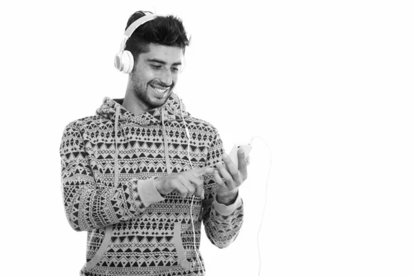 Plan studio de jeune homme persan heureux souriant tout en écoutant de la musique et en utilisant un téléphone portable — Photo