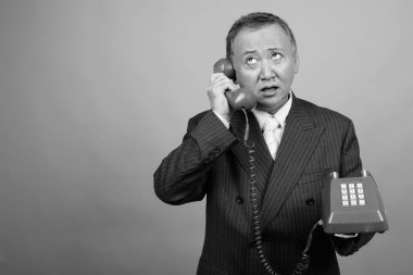 Yetişkin Asyalı iş adamının gri arka plan üzerinde siyah beyaz telefon kullanmasının stüdyo görüntüleri.
