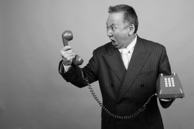 Yetişkin Asyalı iş adamının gri arka plan üzerinde siyah beyaz telefon kullanmasının stüdyo görüntüleri.