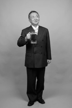 Yetişkin Asyalı iş adamının gri arka planda siyah beyaz bira bardağını tutarken çekilmiş bir fotoğraf.