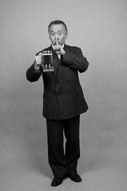 Yetişkin Asyalı iş adamının gri arka planda siyah beyaz bira bardağını tutarken çekilmiş bir fotoğraf.