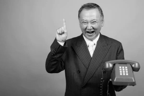 Studioaufnahme Eines Reifen Asiatischen Geschäftsmannes Mit Altem Telefon Vor Grauem — Stockfoto