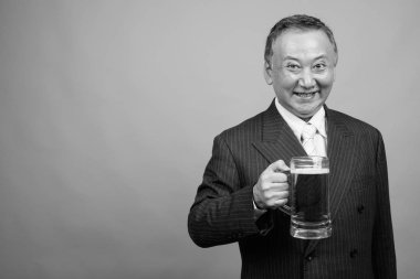 Yetişkin Asyalı iş adamının gri arka planda siyah beyaz bira bardağını tutarken çekilmiş bir fotoğraf.