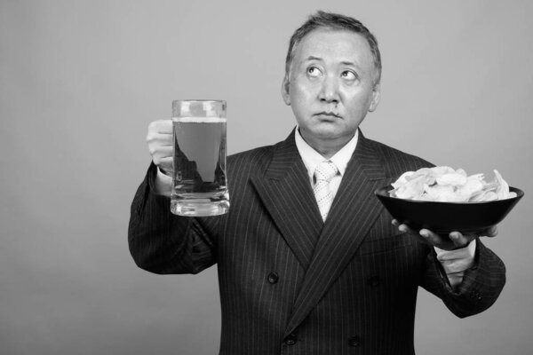 Studio shot of mature Asian businessman in suit against gray background in black and white