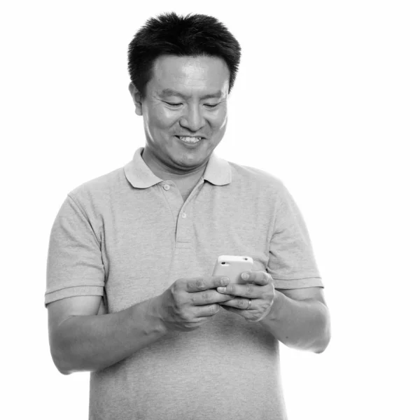 Estudio de tiro de feliz hombre japonés sonriendo mientras se utiliza el teléfono móvil —  Fotos de Stock