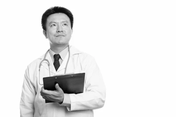 Studio shot of Japanese man doctor holding clipboard while thinking — Stock Photo, Image
