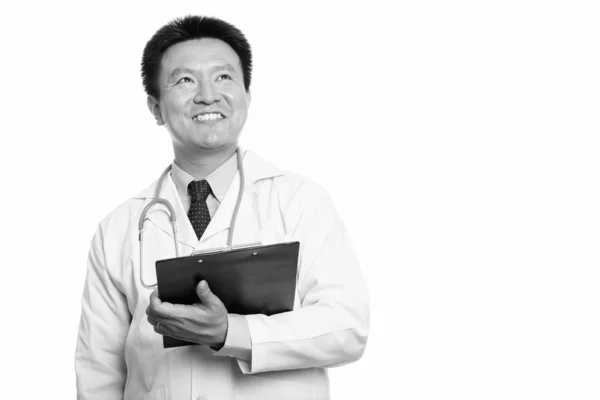 Feliz japonés hombre médico sonriendo mientras sostiene portapapeles y pensando —  Fotos de Stock