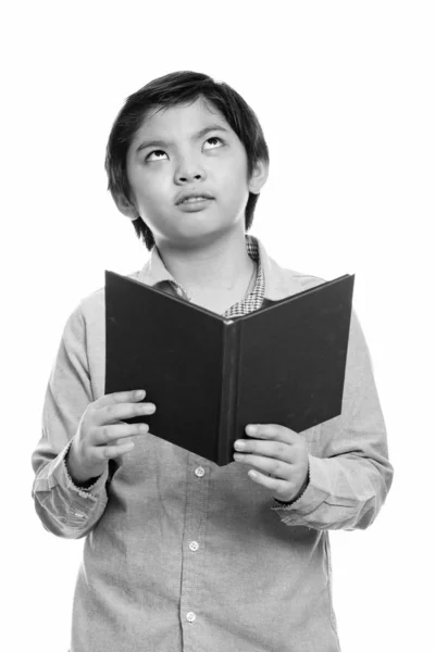 Studio shot of cute Japanese boy holding book while thinking and looking up — Stok Foto