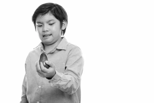 Studio colpo di carino giapponese ragazzo holding avocado e cercando disgustato — Foto Stock