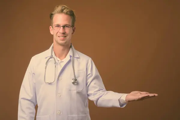 Jovem bonito homem médico contra fundo marrom — Fotografia de Stock