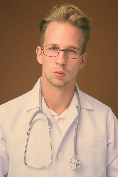 Молодой красивый мужчина врач на коричневом фоне — стоковое фото